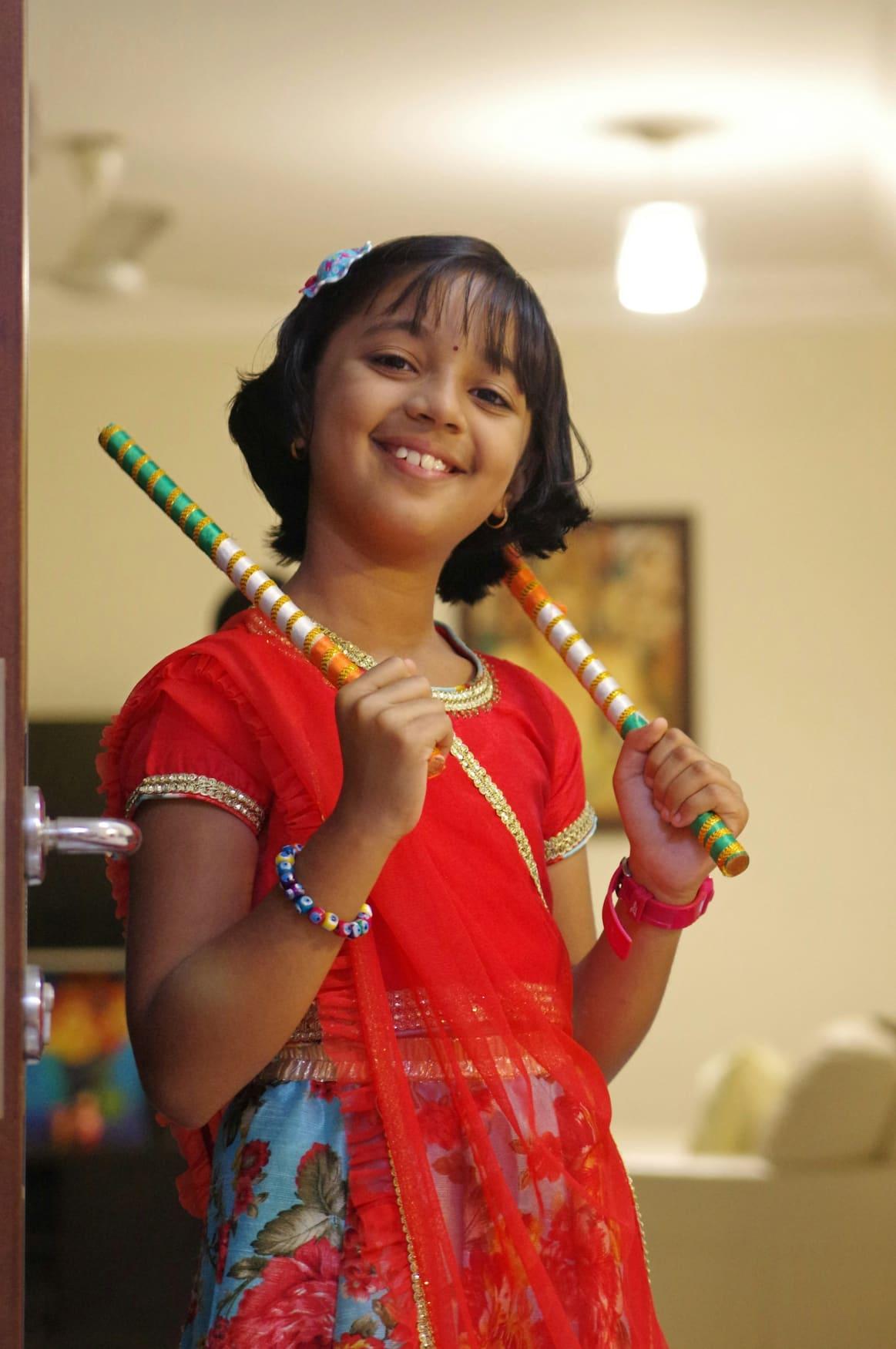 Smiling girl in a red chaniya choli holding dandiya sticks