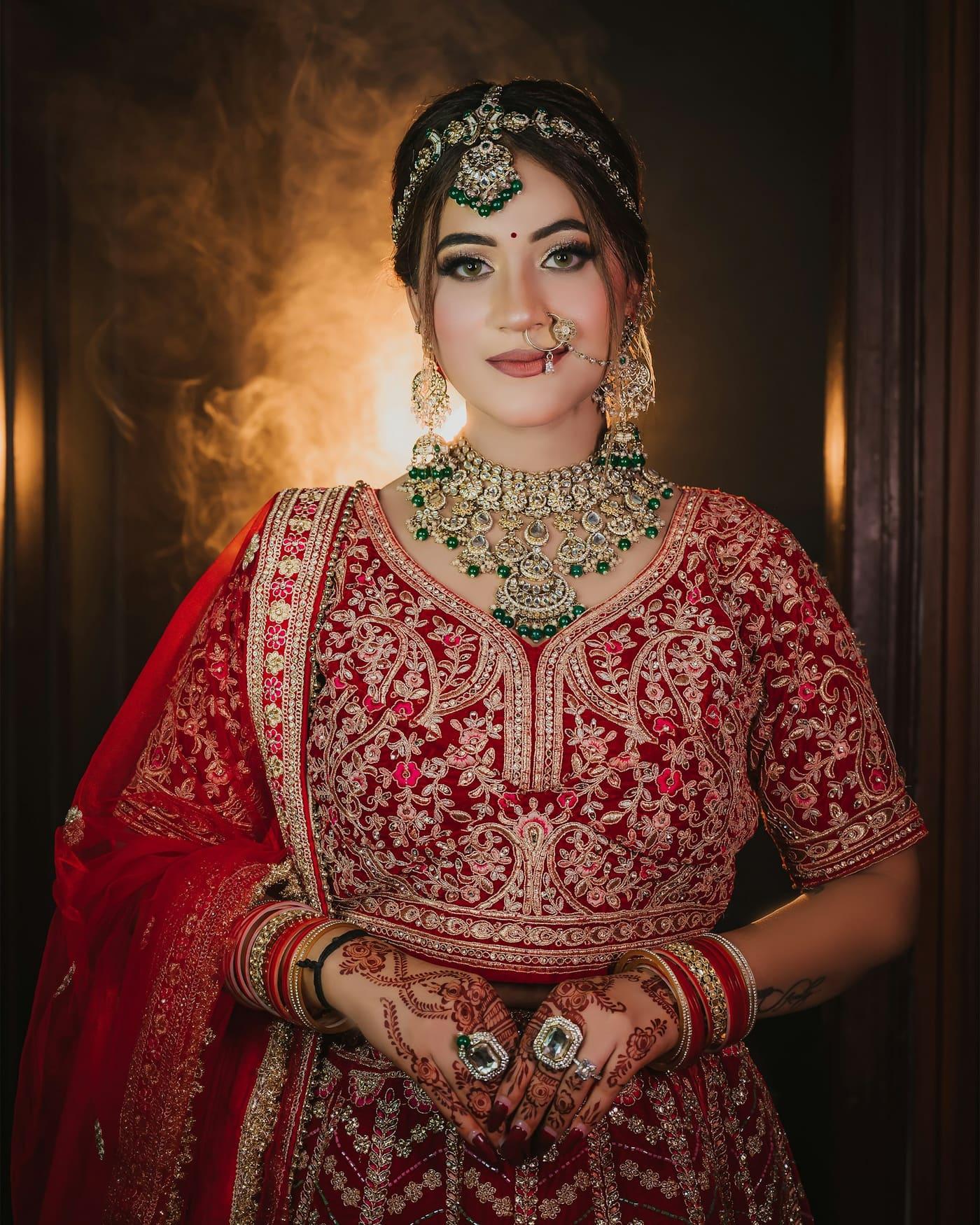 Bride in a red lehenga with gold embroidery and emerald kundan jewellery